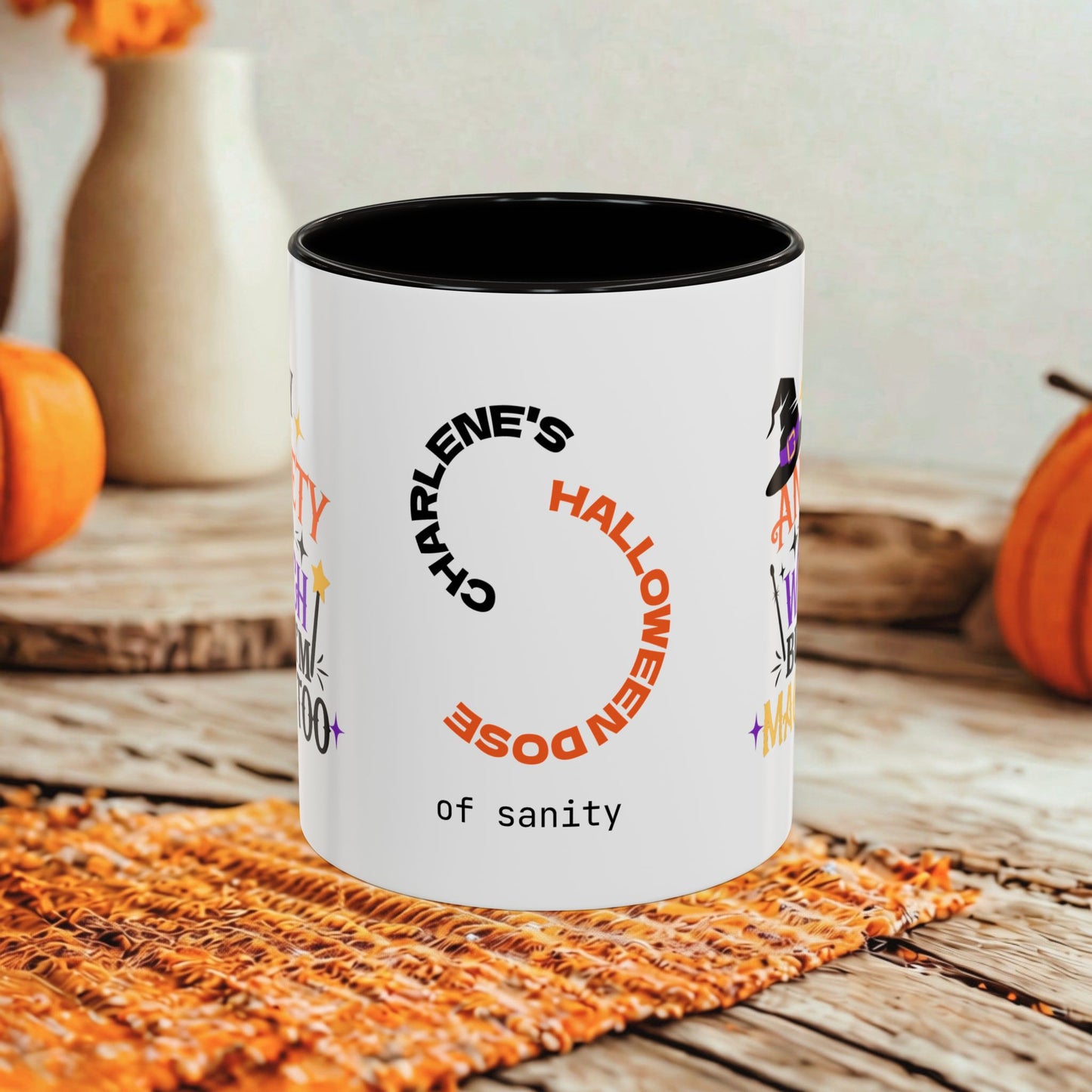 A white ceramic mug with a black interior and rim, printed with Halloween-themed text and graphics including 'CHARLENE'S HALLOWEEN DOSE of sanity' and 'of sanity' at the bottom, styled on a rustic wooden surface with orange pumpkins and a woven mat in the background.