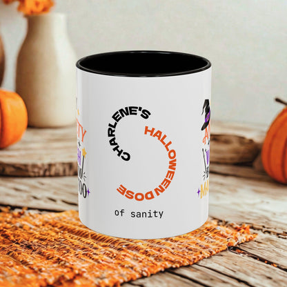 A white ceramic mug with a black interior and rim, printed with Halloween-themed text and graphics including 'CHARLENE'S HALLOWEEN DOSE of sanity' and 'of sanity' at the bottom, styled on a rustic wooden surface with orange pumpkins and a woven mat in the background.