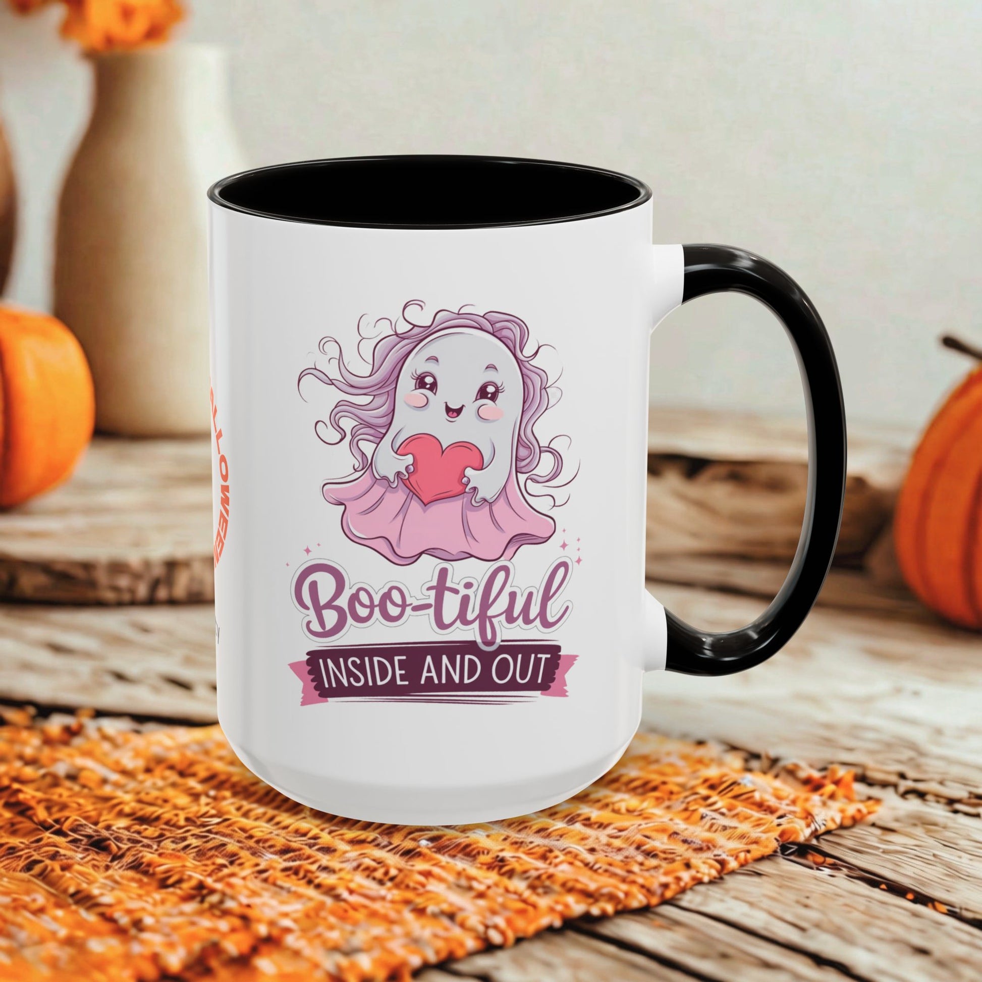 A white ceramic coffee mug with a black handle and interior, featuring a cute cartoon ghost graphic with a pink bow and the text 'Boo-tiful INSIDE AND OUT'. The mug is styled on a rustic wooden table with autumn props including pumpkins and a woven placemat.
