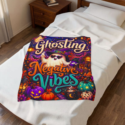 A rectangular Halloween-themed blanket displayed against a light wood plank background. The artwork features the words 'Ghosting Negative Vibes' in large decorative lettering, with a cartoon ghost wearing a witch hat and sunglasses, surrounded by pumpkins, a moonlit sky, a house, and lanterns.