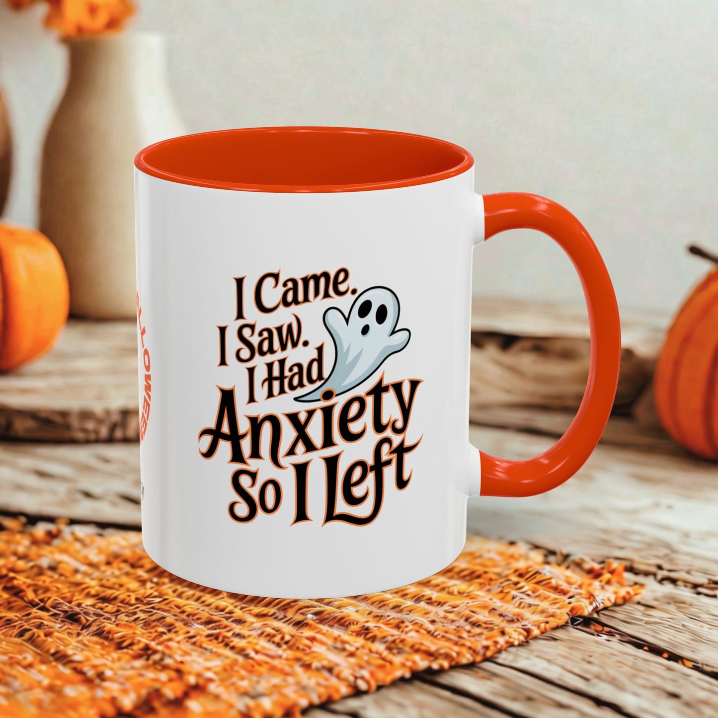 A white ceramic mug with a bright orange interior and handle, featuring a Halloween-themed printed design that reads 'I Came, I Saw, I Had Anxiety So I Left' with a small ghost illustration. The mug is styled on a rustic wooden surface with autumn props in the background.