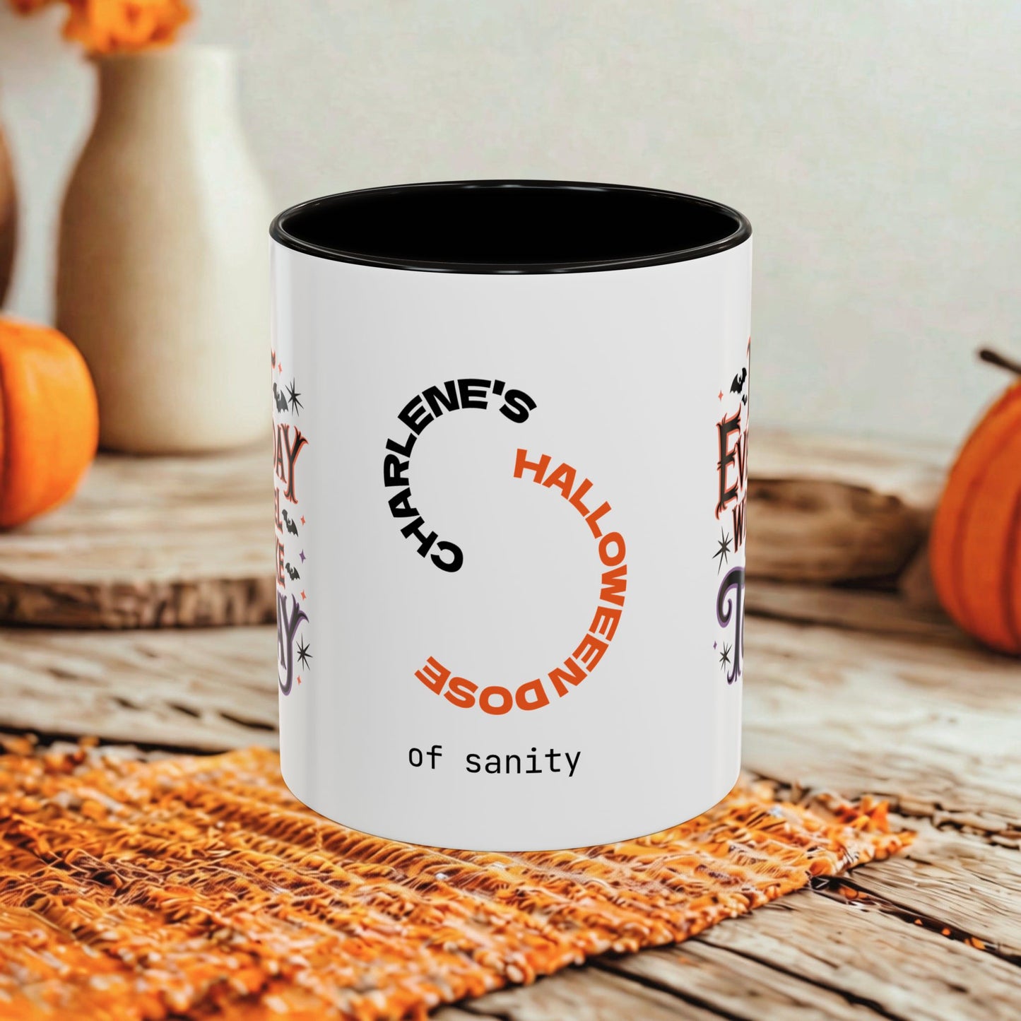 A white ceramic mug with a black interior and printed Halloween-themed text reading 'Charlene's Halloween Dose of sanity,' styled on a rustic wooden surface with pumpkins and a woven mat in the background.