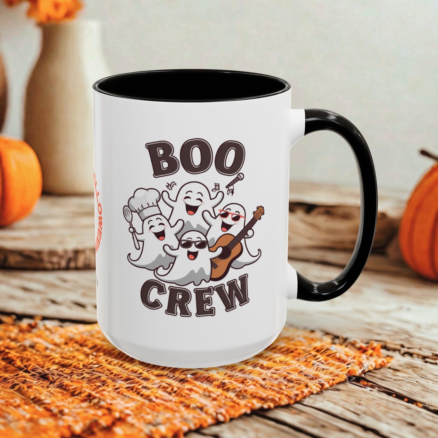 A white ceramic mug with a black handle and interior, printed with the words 'BOO CREW' and a group of smiling cartoon ghosts, shown on a rustic wooden surface with orange pumpkins and a woven placemat in the background.