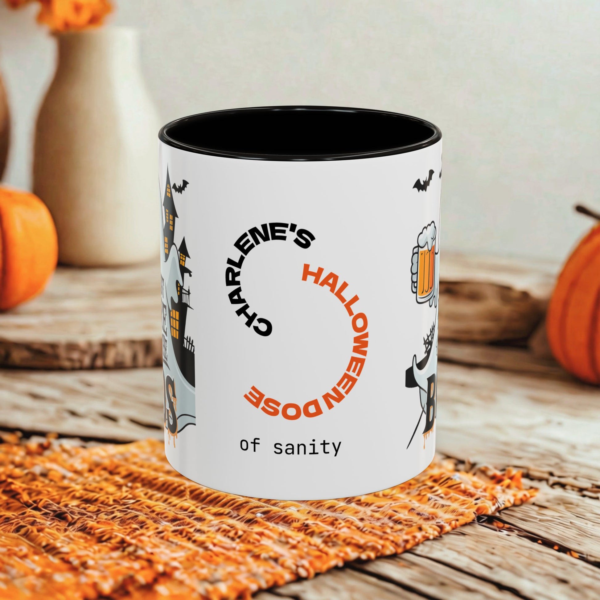 A white ceramic mug with a black interior and Halloween-themed printed graphics, including bats, a witch, a beer mug, and the text 'Charlene's Halloween Dose of sanity,' styled on a rustic wooden surface with pumpkins and a woven mat in the background.