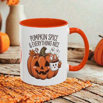 A white ceramic coffee mug with a bright orange handle and interior, featuring a Halloween graphic of a jack-o'-lantern, ghosts, and the text 'PUMPKIN SPICE & EVERYTHING NICE'. The mug is styled on an orange woven placemat over a rustic wooden table with seasonal background props.