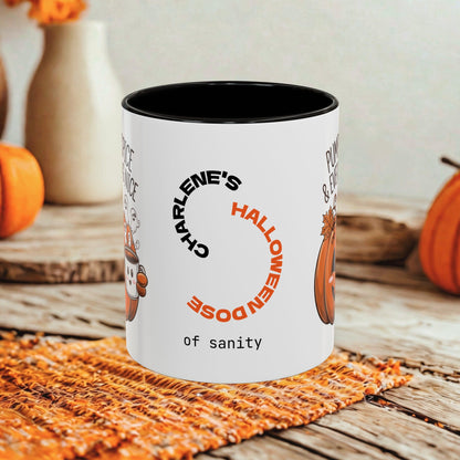 A white ceramic mug with a black interior and printed Halloween-themed text and pumpkin illustrations, set on a rustic wooden surface with pumpkins and a woven mat in the background.