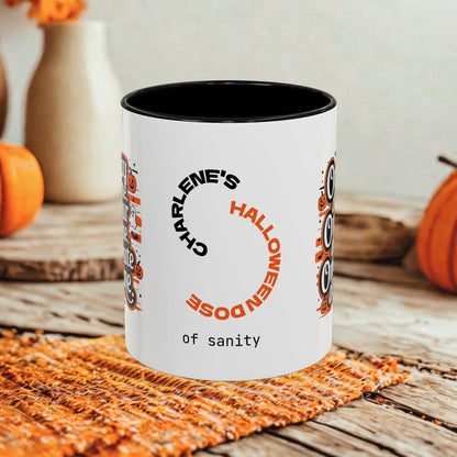 A white ceramic mug with a black interior and rim, printed with a Halloween-themed design featuring the text 'Charlene's Halloween Dose of sanity' and owl illustrations, set on a rustic wooden table with autumn decorations in the background.