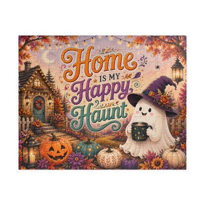 A square decorative puzzle featuring a whimsical Halloween scene with the phrase “Home is my Happy Haunt” in large decorative lettering. The artwork shows a cozy house, glowing lanterns, pumpkins, flowers, and a smiling ghost wearing a witch hat and holding a mug.