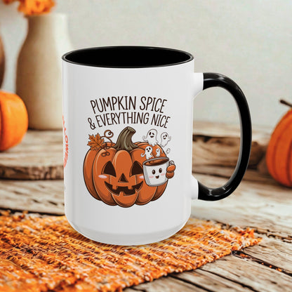 A white ceramic mug with a black handle and interior, featuring a cartoon pumpkin, ghosts, and the text 'PUMPKIN SPICE & EVERYTHING NICE' on the front. The mug is styled on a woven orange placemat over a rustic wooden surface with blurred orange pumpkins and a beige vase in the background.