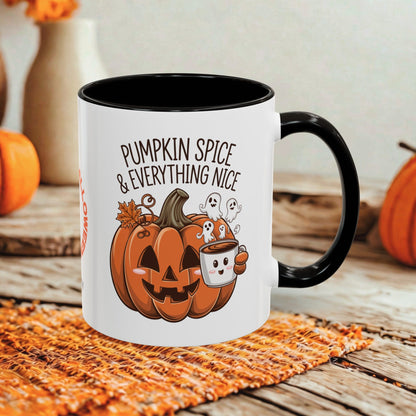 A white ceramic mug with a black handle and interior, printed with a Halloween design featuring a jack-o'-lantern, ghosts, and the text 'PUMPKIN SPICE & EVERYTHING NICE.' The mug is styled on a woven orange placemat over a rustic wooden surface, with blurred pumpkins and a vase in the background.