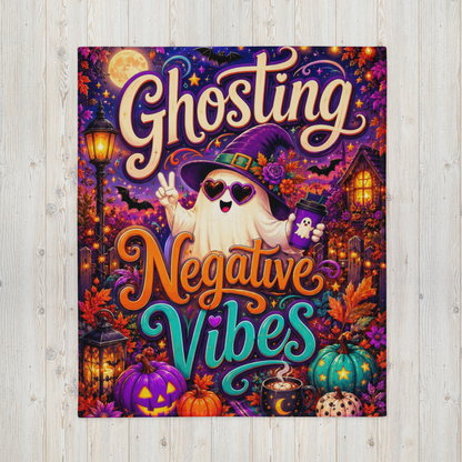 A rectangular Halloween-themed blanket displayed against a light wood plank background. The artwork features the words 'Ghosting Negative Vibes' in large decorative lettering, with a cartoon ghost wearing a witch hat and sunglasses, surrounded by pumpkins, a moonlit sky, a house, and lanterns.