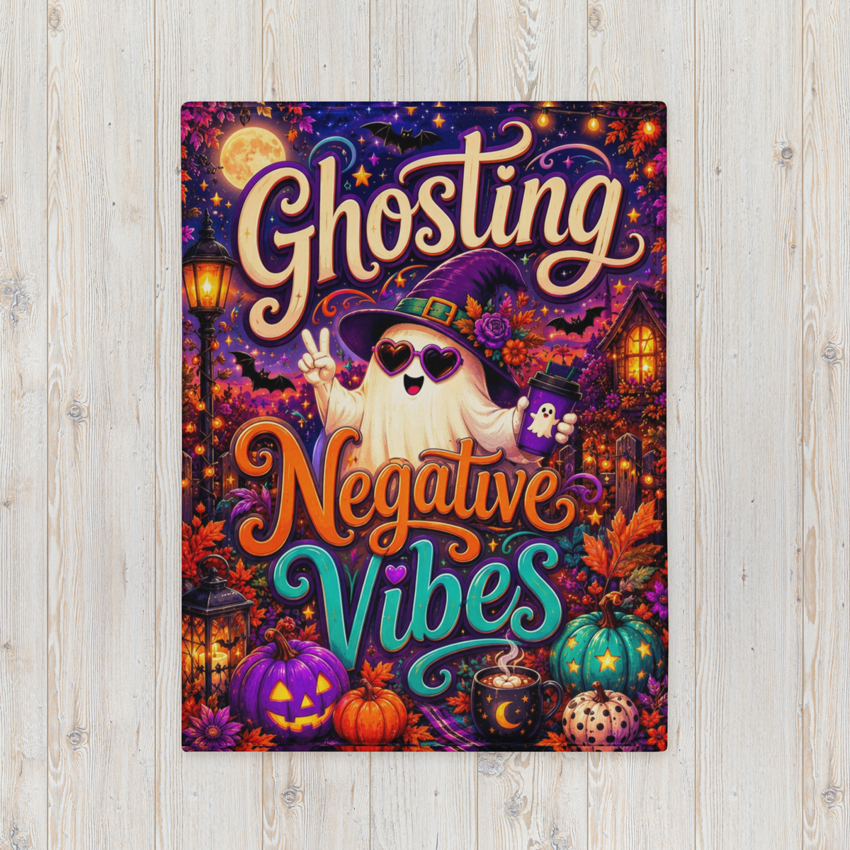 A rectangular Halloween-themed blanket displayed against a light wood plank background. The artwork features the words 'Ghosting Negative Vibes' in large decorative lettering, with a cartoon ghost wearing a witch hat and sunglasses, surrounded by pumpkins, a moonlit sky, a house, and lanterns.