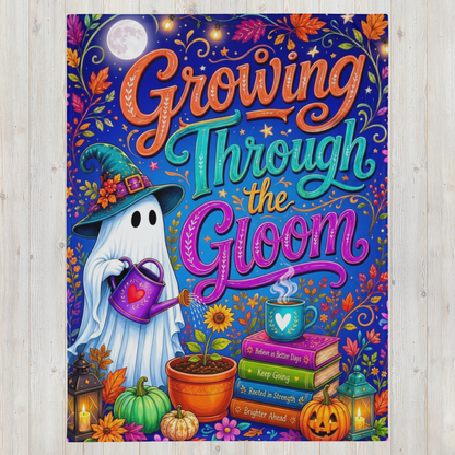 A colorful blanket featuring the quote 'Growing Through the Gloom' in stylized lettering, with a ghost in a witch hat watering a plant, surrounded by pumpkins, flowers, books, and lanterns, shown against a light wood background.