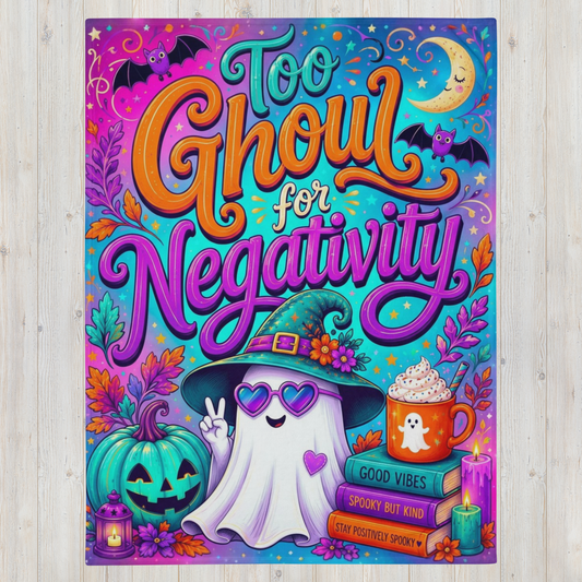 A colorful Halloween-themed blanket with the phrase 'Too Ghoul for Negativity' in large stylized lettering. The design features a smiling ghost wearing a witch hat, a jack-o'-lantern, a mug of hot chocolate, candles, bats, a crescent moon, and autumn leaves on a bright multicolor background, shown against a light wood surface.