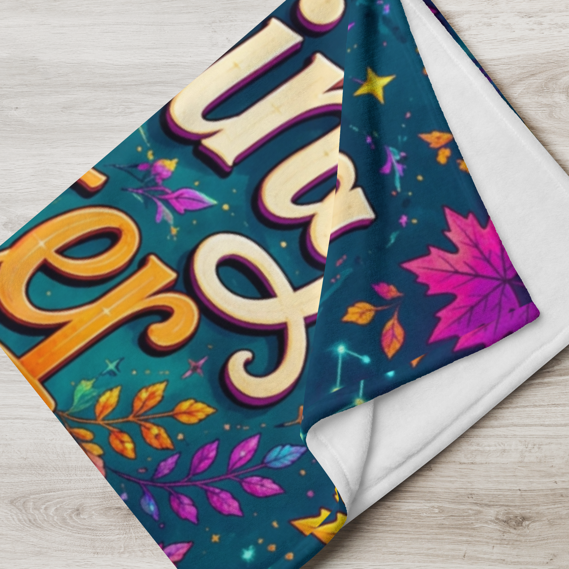 A folded blanket with a colorful Halloween-themed print featuring the word 'Brewing Better Days' in large cream letters, purple maple leaves, yellow stars, and orange leaves on a dark teal background, shown on a light wood surface.