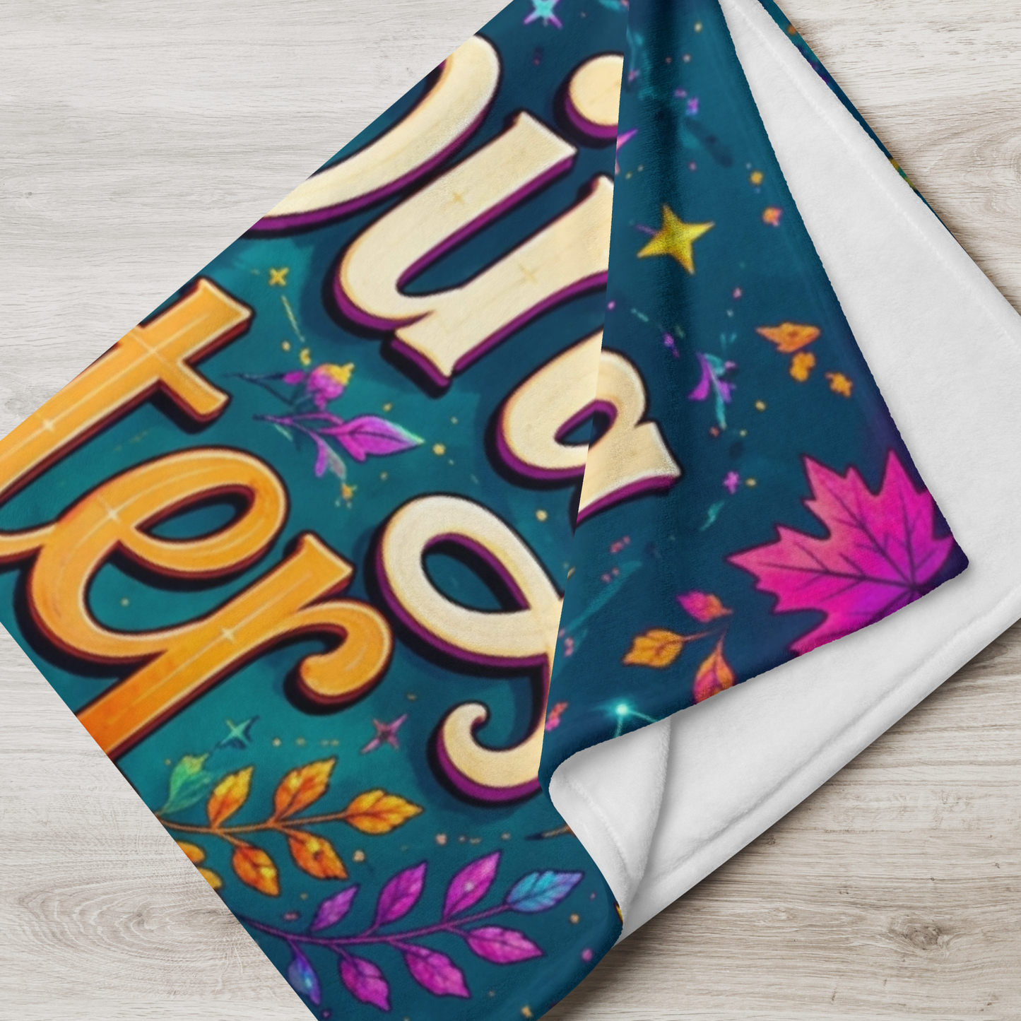 A folded throw blanket with a colorful Halloween-themed design featuring the words 'Brewing Better Days' in large cream and gold letters on a teal background with leaves and stars, shown on a light wood floor.