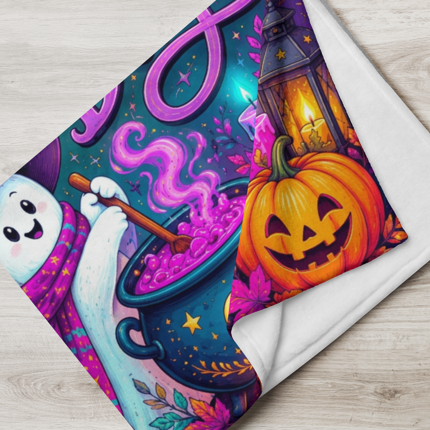 A folded blanket with a colorful Halloween-themed printed design, shown on a light wood surface. The print features a smiling ghost, a glowing lantern, a jack-o'-lantern pumpkin, and a cauldron of purple potion.