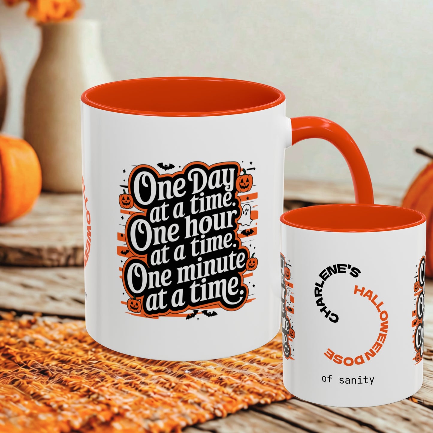 A white ceramic Halloween-themed mug with an orange interior and handle, shown alongside a smaller matching cup. The larger mug features the text 'One Day at a time.