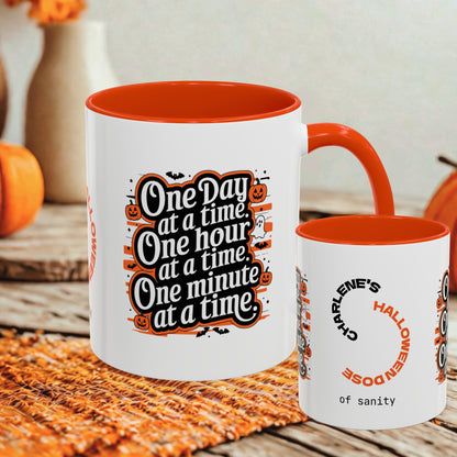 A white ceramic Halloween-themed mug with an orange interior and handle, shown alongside a smaller matching cup. The larger mug features the text 'One Day at a time.