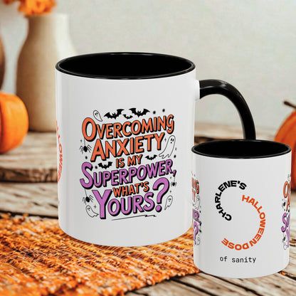 Two white ceramic mugs with black interiors and handles are shown on a rustic table with autumn decor in the background. The larger mug features the phrase 'Overcoming Anxiety Is My Superpower, What's Yours?' in orange, purple, and black lettering, while the smaller mug reads 'Charlene's Halloween Doze of sanity' with a circular arrow graphic.