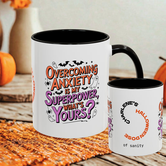 Two white ceramic mugs with black interiors and handles are shown on a rustic table with autumn decor in the background. The larger mug features the phrase 'Overcoming Anxiety Is My Superpower, What's Yours?' in orange, purple, and black lettering, while the smaller mug reads 'Charlene's Halloween Doze of sanity' with a circular arrow graphic.