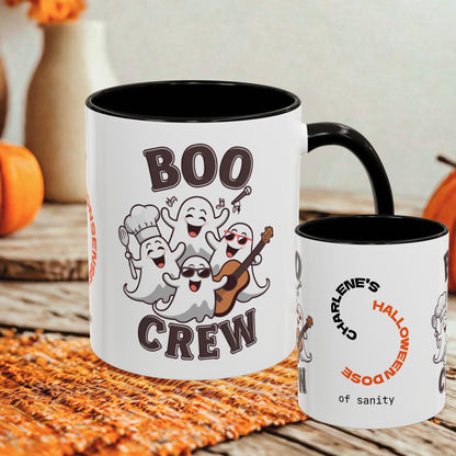 Two white ceramic mugs with black interiors and handles are shown on a rustic wooden surface with autumn props. The larger mug features a cartoon group of ghosts singing and the words “BOO CREW,” while the smaller mug shows partial text including “CHARLENE’S HALLOWEEN DOSE of sanity.