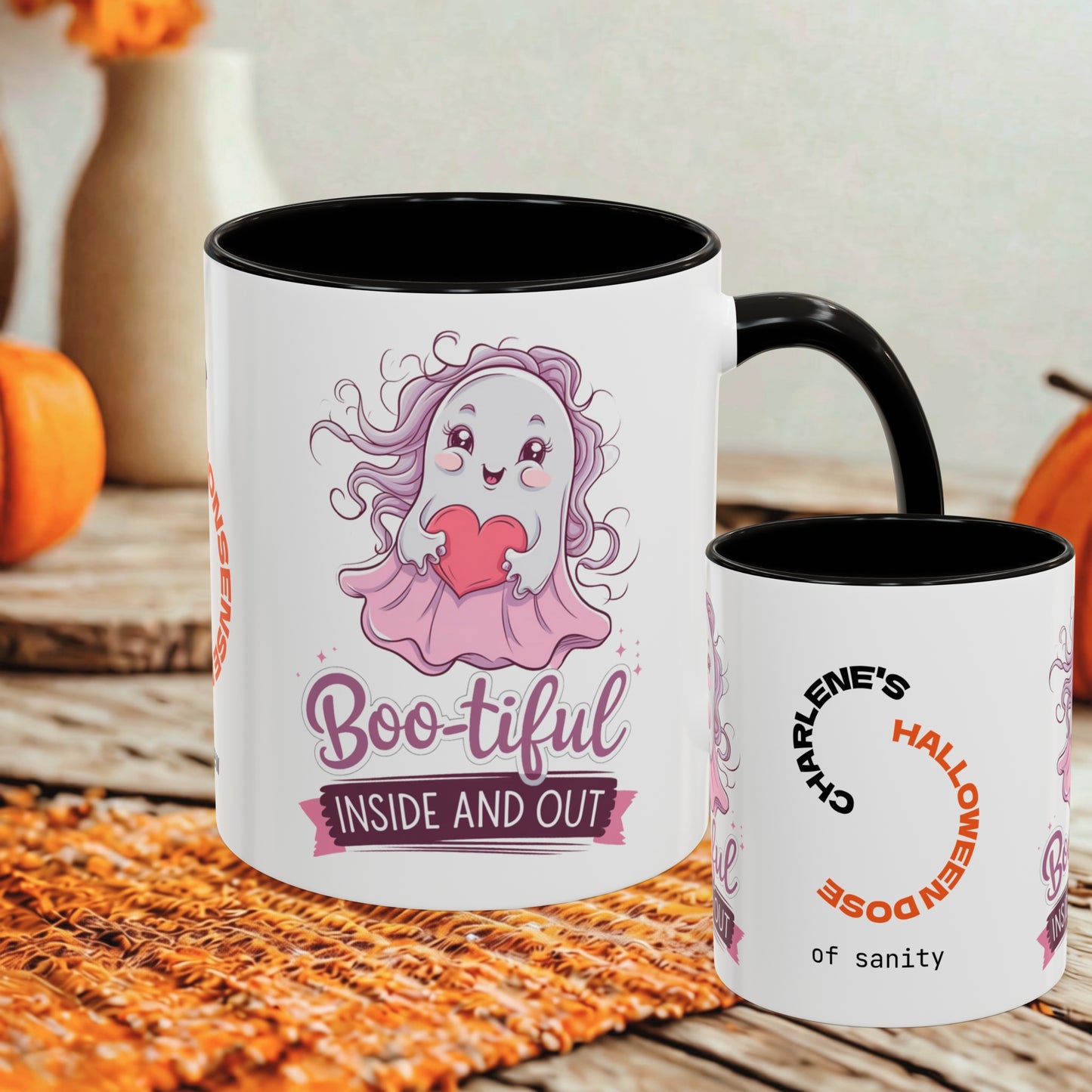 Two white ceramic mugs with black interiors and handles, displayed on a rustic wooden surface with autumn props. The larger mug features a cute cartoon ghost character in pink holding a red heart, with the text 'Boo-tiful INSIDE AND OUT'.
