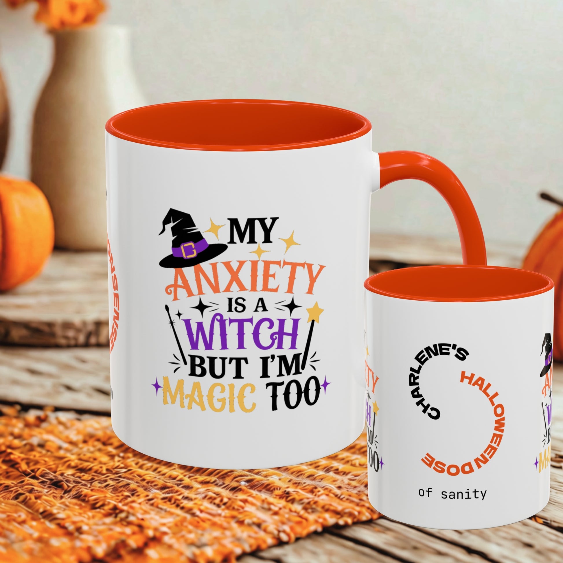 A white ceramic mug with a bright orange interior and handle, printed with a Halloween-themed quote and witch hat graphic, shown alongside a smaller matching mug on a rustic wooden surface with autumn decor in the background.