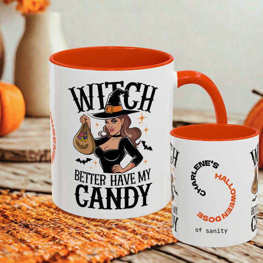 A white ceramic Halloween mug with a bright orange interior and handle, featuring a witch illustration and the text 'WITCH BETTER HAVE MY CANDY' on the front. A smaller matching mug is shown beside it on a rustic table with autumn decor in the background.