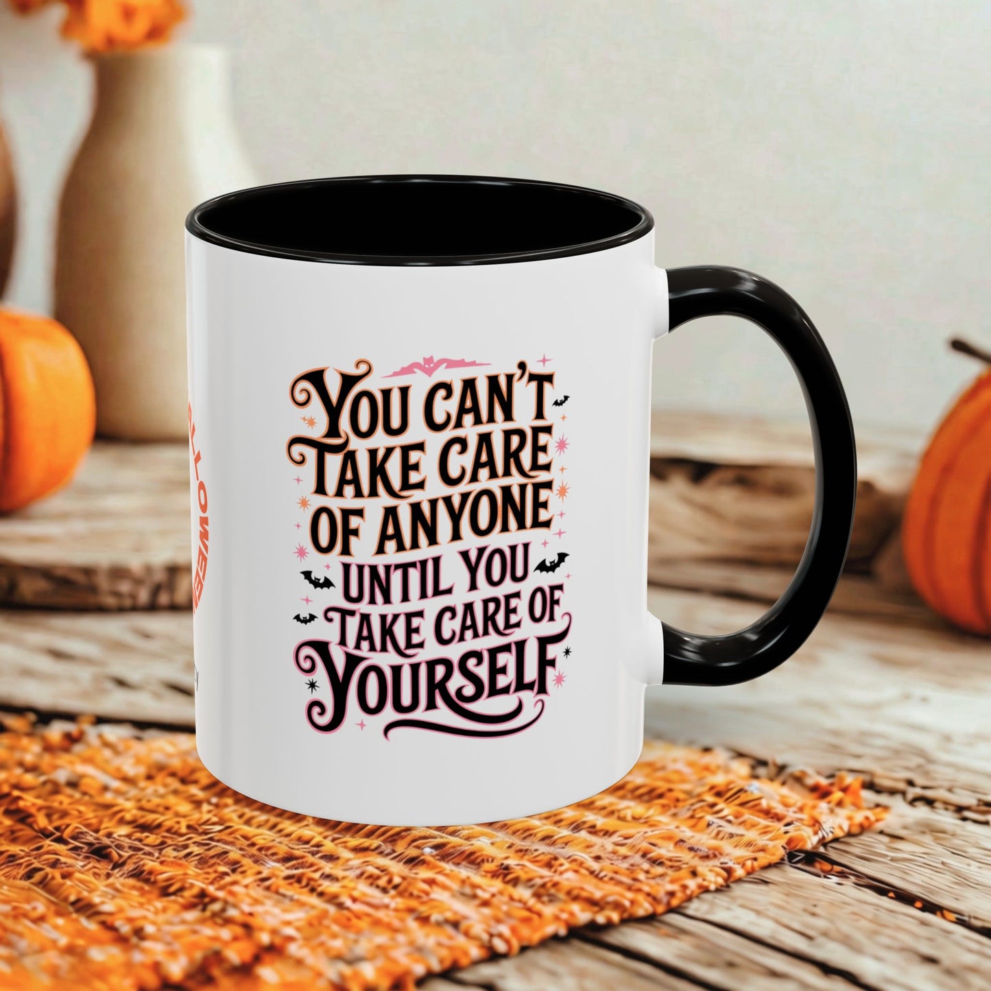 A white ceramic coffee mug with a black handle and interior, featuring a decorative quote printed on the front. The mug is styled on a rustic wooden table with autumn props, including pumpkins and a woven placemat.