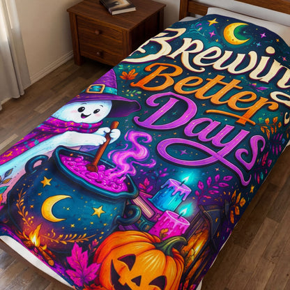 A colorful Halloween-themed blanket, displayed on a bed in a bedroom setting. The design features a whimsical cartoon witch stirring a glowing cauldron with the text 'Brewing Better Days' in stylized fonts, alongside a jack-o'-lantern, candles, and a crescent moon.