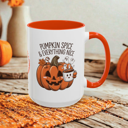 A white ceramic mug with a bright orange handle and interior, featuring a Halloween-themed graphic that reads 'Pumpkin Spice & Everything Nice' above a jack-o'-lantern, marshmallow, and small ghosts. The mug is styled on a woven orange placemat over a rustic wooden surface with blurred pumpkins in the background.