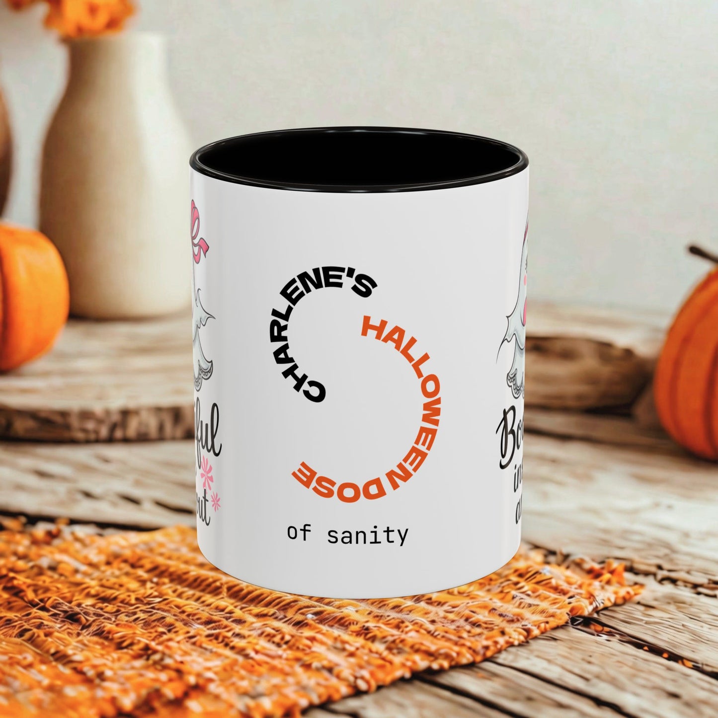 A white ceramic mug with a black interior and rim, printed with the phrase 'Charlene's Halloween Dose of sanity' in black and orange text. The mug is styled on a rustic wooden table with autumn props including pumpkins and a woven placemat.