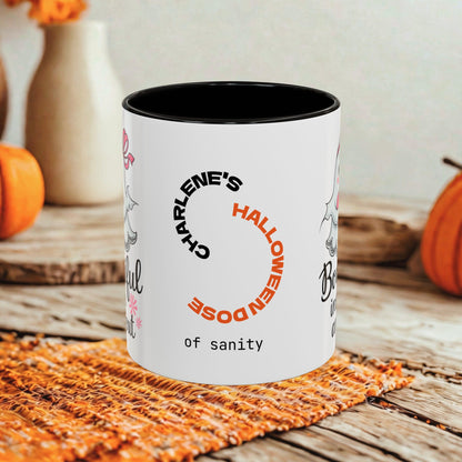 A white ceramic mug with a black interior and rim, printed with the phrase 'Charlene's Halloween Dose of sanity' in black and orange text. The mug is styled on a rustic wooden table with autumn props including pumpkins and a woven placemat.