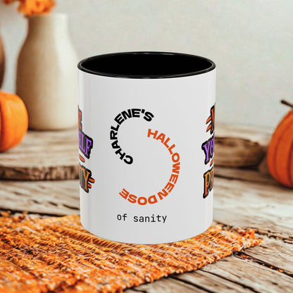 A white ceramic mug with a black interior, printed with the phrase 'Charlene's Halloween Dose of sanity' in black and orange text, styled on a rustic wooden table with autumn decorations in the background.