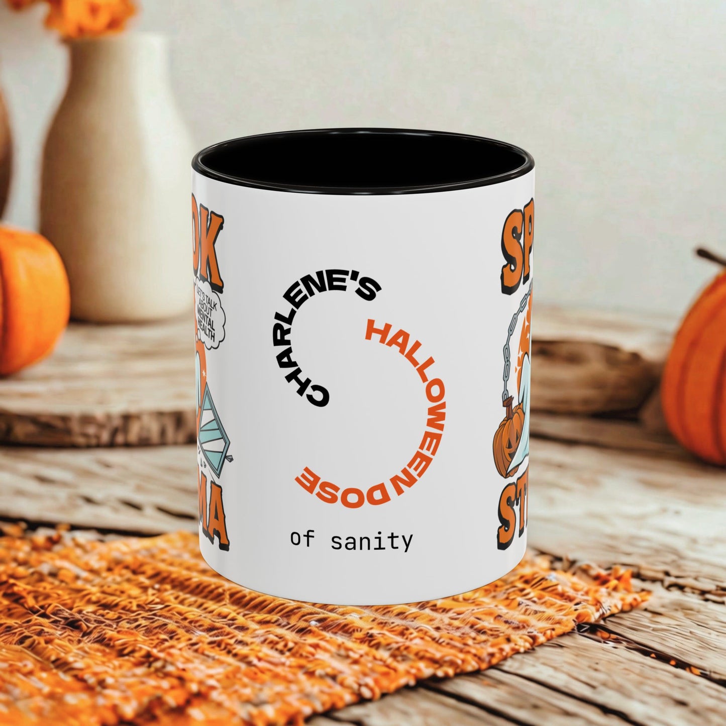 A white ceramic mug with a black interior, featuring a Halloween-themed graphic that reads 'Charlene's Halloween Dose of sanity' in black and orange text. The mug is styled on a rustic wooden table with autumn props including pumpkins and a woven placemat.
