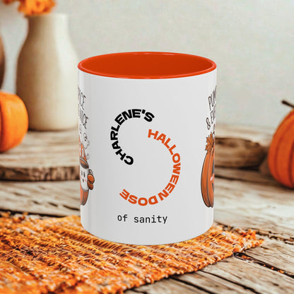 A white ceramic mug with a bright orange interior, featuring a Halloween-themed printed design with the text 'CHARLENE'S HALLOWEEN DOSE of sanity' and pumpkin illustrations, set on a rustic wooden table with autumn decorations in the background.