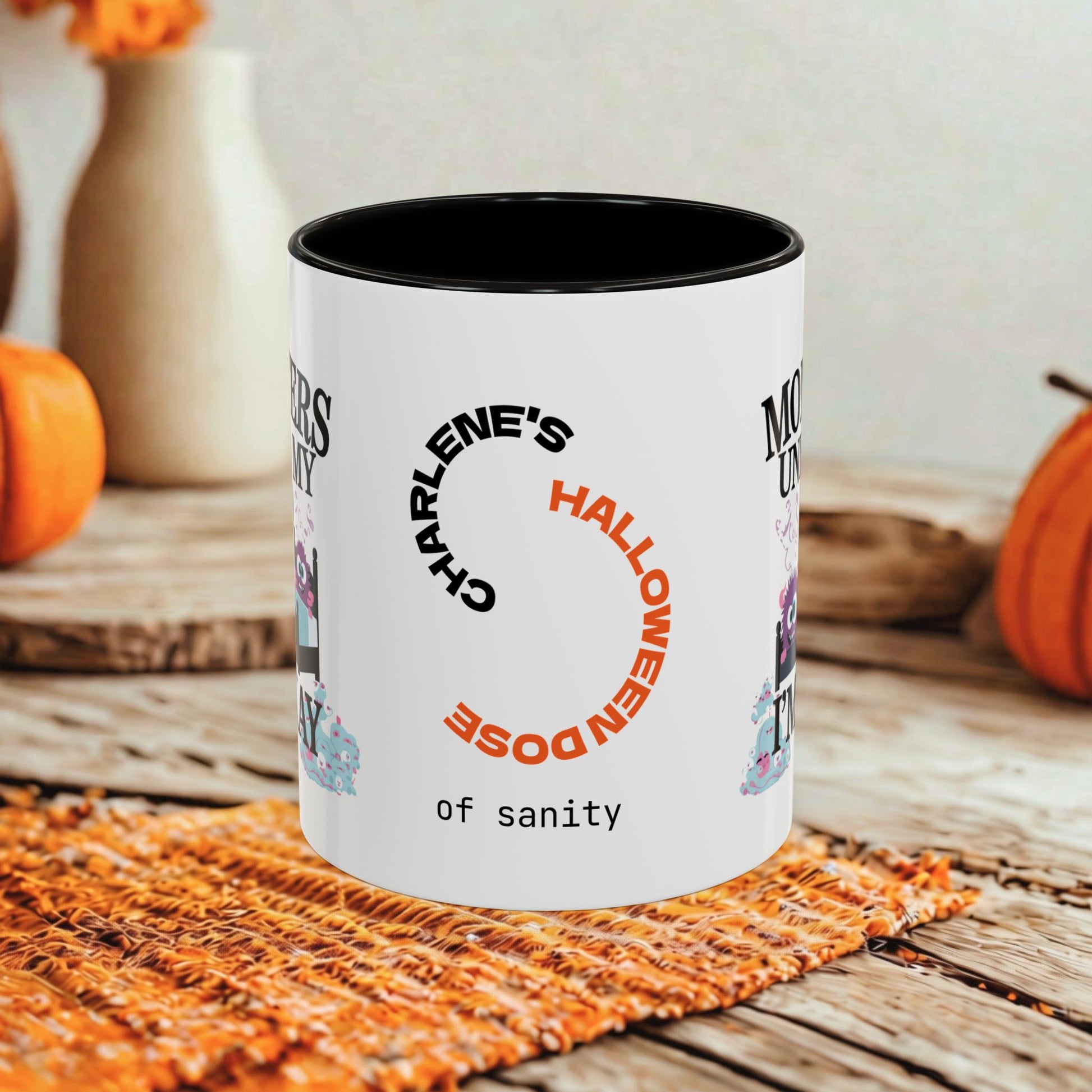 A white ceramic mug with a black interior and custom Halloween-themed printed text reading 'Charlene's Halloween Dose of sanity,' styled on a rustic wooden surface with orange pumpkins and a woven mat in the background.