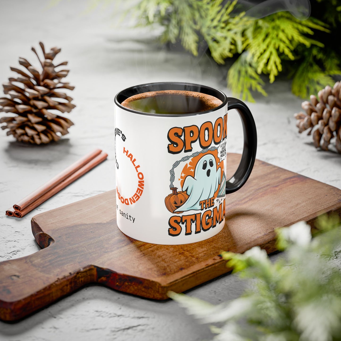 A white ceramic mug with a black handle and rim sits on a wooden cutting board. The mug is printed with a Halloween graphic featuring orange text reading 'SPOOK THE STIGMA' and an orange pumpkin with a white ghost.