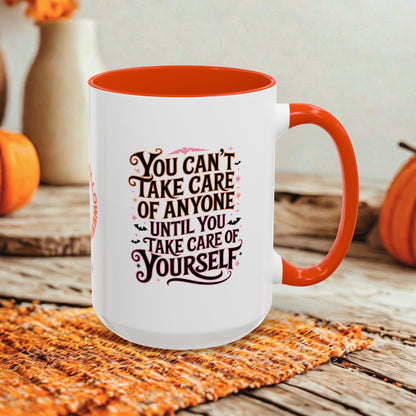 A white ceramic mug with a bright orange handle and interior, featuring the printed phrase 'YOU CAN'T TAKE CARE OF ANYONE UNTIL YOU TAKE CARE OF YOURSELF' in dark brown lettering. The mug is styled on a woven orange placemat over a rustic wooden table, with decorative pumpkins and a neutral background.