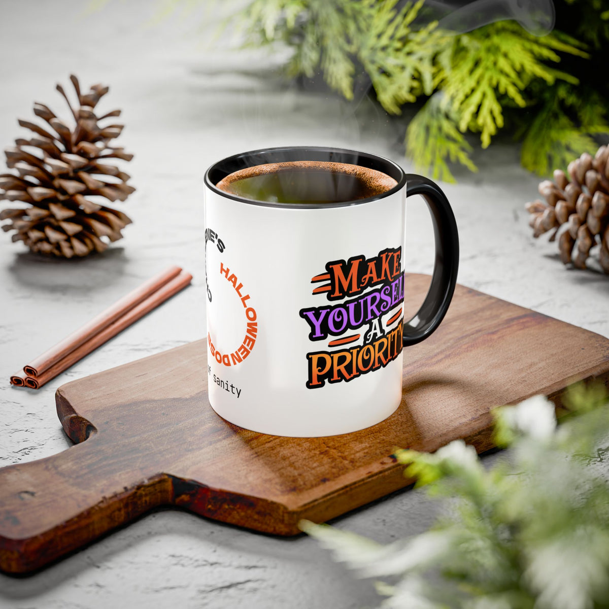 A white ceramic coffee mug with a black handle and rim sits on a wooden cutting board. The mug features a Halloween-themed graphic with the text 'MAKE YOURSELF A PRIORITY' in orange, purple, and black lettering.