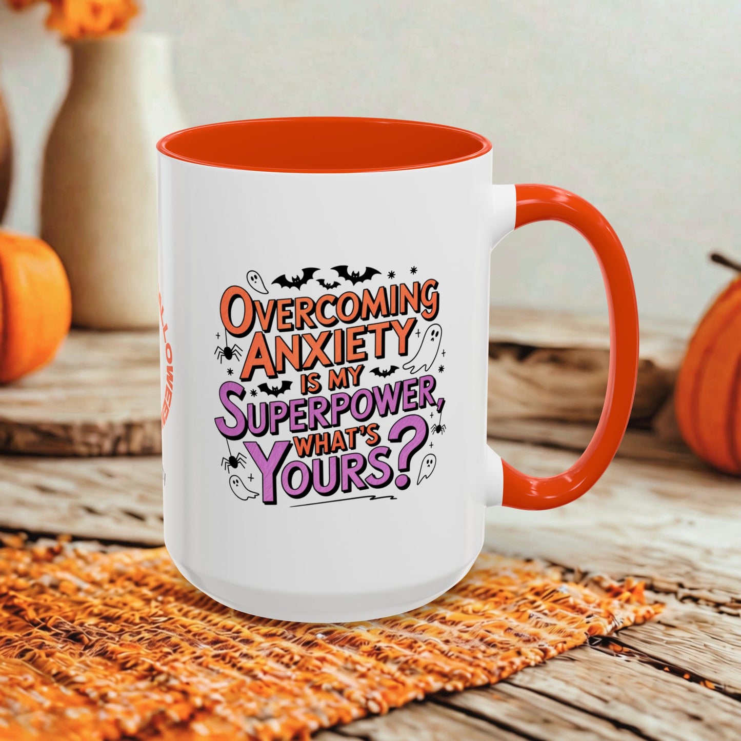 A white ceramic mug with a bright orange handle and interior, featuring the printed phrase 'Overcoming Anxiety is my Superpower, What's Yours?' in orange and purple lettering. The mug is styled on a rustic wooden surface with a woven orange placemat and autumn-themed background elements.