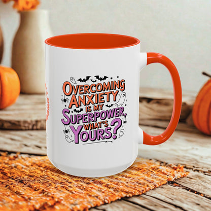 A white ceramic mug with a bright orange handle and interior, featuring the printed phrase 'Overcoming Anxiety is my Superpower, What's Yours?' in orange and purple lettering. The mug is styled on a rustic wooden surface with a woven orange placemat and autumn-themed background elements.