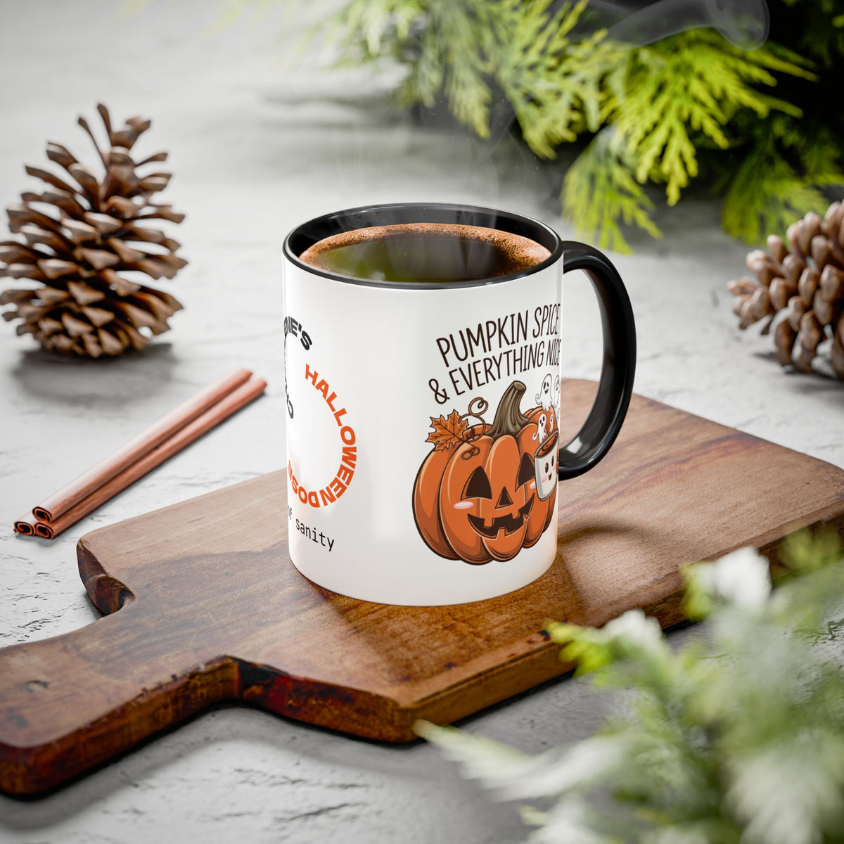 A white ceramic coffee mug with a black handle and rim sits on a wooden cutting board. The mug features a Halloween-themed graphic with jack-o'-lanterns and the text 'PUMPKIN SPICE & EVERYTHING NICE'.