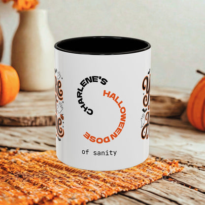 A white ceramic mug with a black interior, featuring a Halloween-themed printed design with the text 'CHARLENE'S HALLOWEEN DOSE of sanity' in black and orange, styled on a rustic wooden table with autumn props.