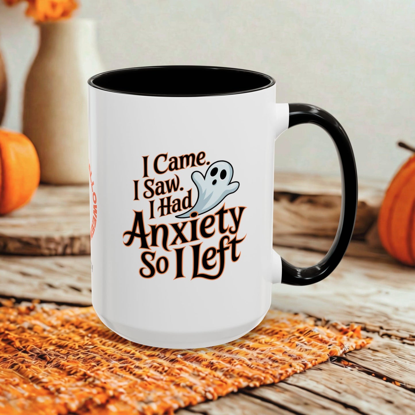 A white ceramic coffee mug with a black interior and handle, featuring a Halloween graphic that reads 'I Came, I Saw, I Had Anxiety So I Left' with a small ghost illustration. The mug is styled on a woven orange placemat on a rustic wooden table with pumpkins in the background.